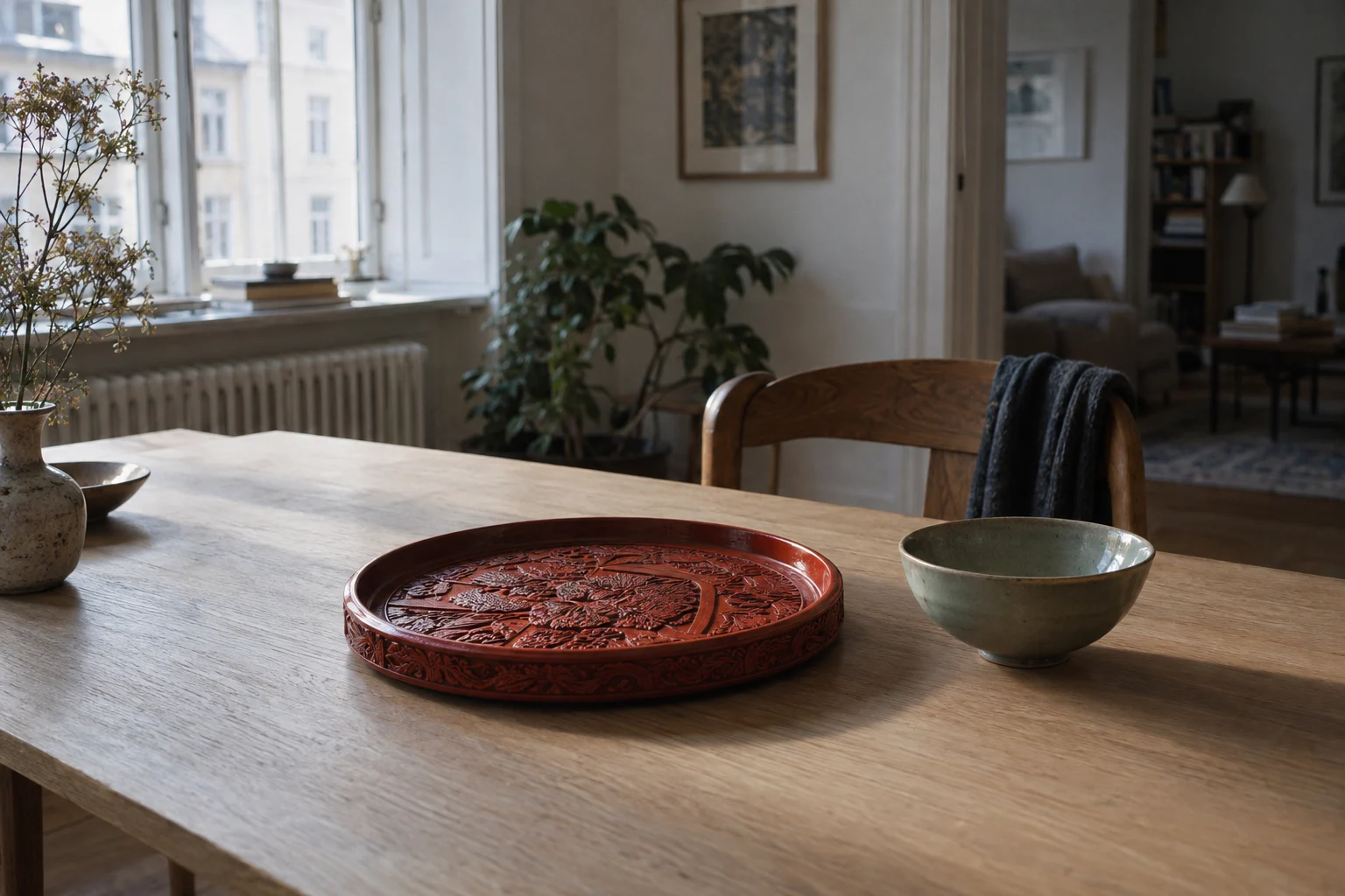 A cinnabar-red lacquer tray on a pale Scandinavian oak table in a Copenhagen apartment, soft northern window light, a celadon bowl beside it