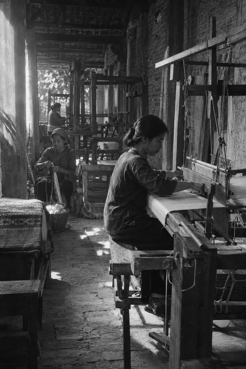 Archive black-and-white photograph from the mid-twentieth century, faded and grainy: the wooden loom in Vạn Phúc, hand-loomed silk, villagers in simple work clothes, old brick and timber
