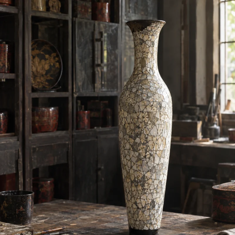 Eggshell vase, tall: A tall slender vase covered in crazed duck-eggshell inlay under clear lacquer, cream and grey mosaic, on turned jackfruit wood, in the Hạ Thái lacquer workshop, dark wooden drying cabinets behind, palette of brown-black, cinnabar and dull gold, by Đỗ Thị Hương