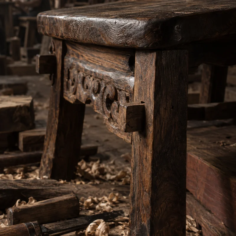 Low stool, carved ironwood, close-up of a pegged mortise-and-tenon joint, no nails, in a Đồng Kỵ carving workshop, ironwood and rosewood planks, chisels and shavings, oiled dark grain, timber-yard light